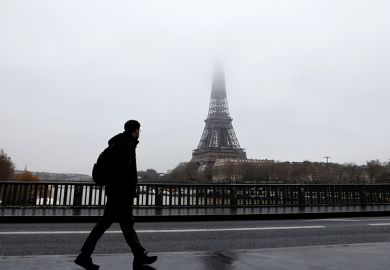 A man walks on a bridge across the Seine with the Eiffel Tower in the background