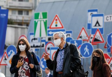 People in face masks in front of signs People in face masks in front of signs