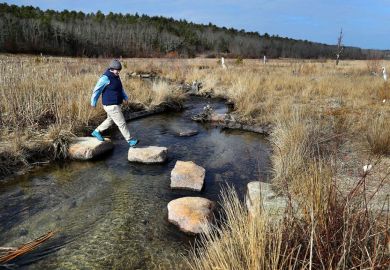 A woman walking across stepping stones in Plymouth, MA, USA. To illustrate College Unbound developing personalised lifelong degree plans for adults with some college credits but no degree.