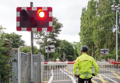 A cyclist stops at a red light at a level crossing to illustrate PhD enrolment hangs on an email
