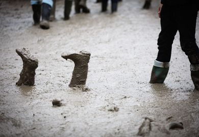 Festival goers in the rain and mud at the Glastonbury Festival, with boots upside down. To illustrate students could be left stranded if a major UK university went bust.
