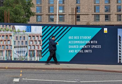 A member of the public walks past a bright and colourful construction hoarding advertising a development of rental student accommodation with shared amenity spaces and retail units in Leeds, UK