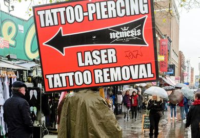 Person holding sign advertising tattoo, piercing and tattoo removal services, Camden High street, London, UK