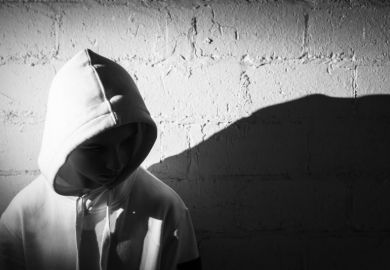 Teenage boy with his hood up against a white brick wall