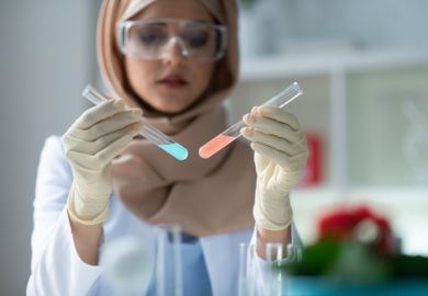 A woman holds up two test tubes containing differently coloured liquids
