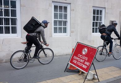 Two delivery couriers ignore a cyclist's dismount sign