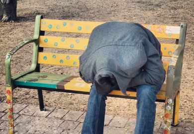 person hiding their head in their coat, sitting on a bench