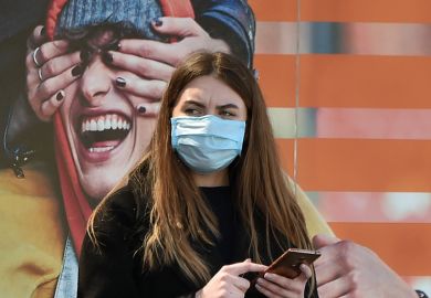 A woman wearing a face mask stands by an advertising placard showing someone having their eyes covered, April 21, 2020 A woman wearing a face mask stands by an advertising placard showing someone having their eyes covered, April 21, 2020