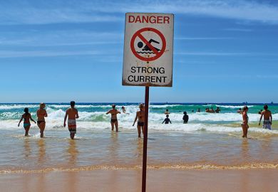 People in the sea at Manly beach, Australia with "dangerous currents" sign.