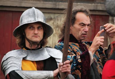 Background actor takes a picture using a smart phone next to another background actor dressed as a medieval guard