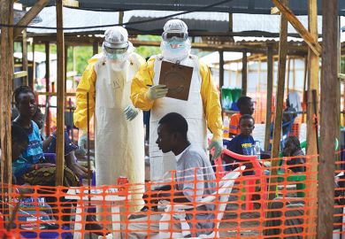 An MSF medical worker, wearing protective clothing relays patient details and updates behind a barrier to a colleague at an MSF facility in Kailahun, 2014. Kailahun along with Kenama district is at the epicentre of the world's worst Ebola outbreak