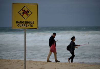 Visitors walk on Bondi beach next to a warning sign for dangerous sea currents on a stormy day in Sydney Visitors walk on Bondi beach next to a warning sign for dangerous sea currents on a stormy day in Sydney