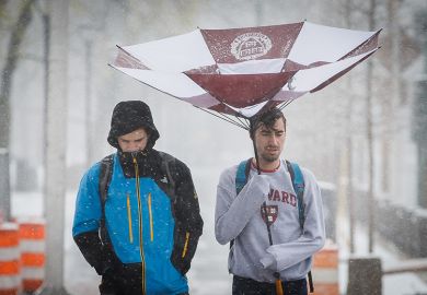 Harvard University students walk under a damaged umbrella near Harvard Square in Cambridge, MA in April