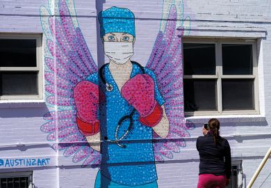 A woman shoots a picture of a mural depicting a medical worker with a mask covering her mouth and nose, wearing boxing gloves and angel-like wings on her back is seen on April 14, 2020 in downtown Denver, United States