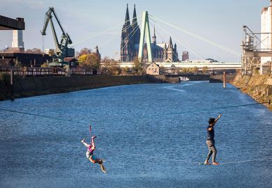 man and woman on slacklines in the Rhine harbour in the district Deutz, in the background the cathedral and Severins bridge, Cologne, Germany man and woman on slacklines in the Rhine harbour in Deutz, with the cathedral and Severins bridge in the background, Cologne, Germany, as a metaphor for European universities balancing cost and ambition