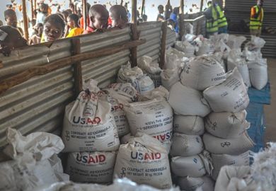 Congolese refugees look through a corrugated metal fence at the final batches of food delivered by the now-dismantled USAID in May 2025