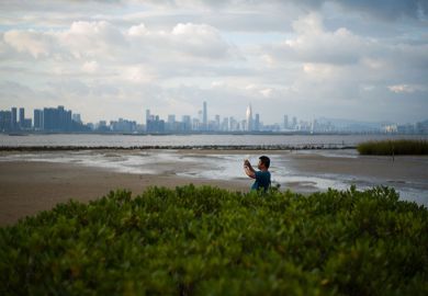 A man takes a photo from the shoreline of Hong Kong’s Deep Bay with the skyline of Chinese mainland city of Shenzhen visible behind him