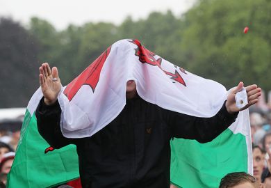 A Wales fan in the rain with flag covering his head. To illustrate that changes to student finance pledged by the front runners in the upcoming Welsh election may be unworkable.