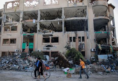 Palestinians walks past the destroyed building of the Islamic University in Gaza City to illustrate Academia in Gaza ‘has been destroyed’ by Israeli ‘educide’