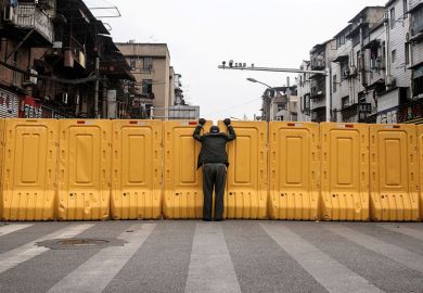 A man wearing a face mask talks to another man through a makeshift barricade wall in Wuhan, Hubei, China as a metaphor for China and Japan to keep borders shut for another term