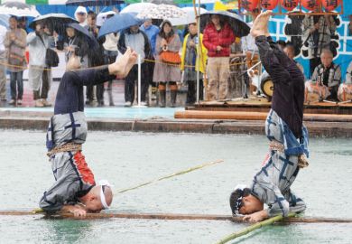 Two performers stand on their heads on a floating square lumbers at a local festival in Tokyo to illustrate academics ‘reluctant’ to recommend Japan as borders stay shut