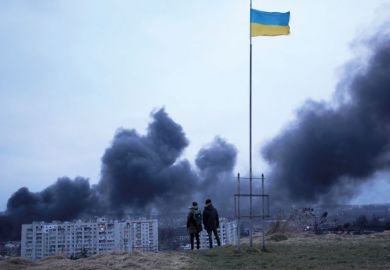 People standing near a Ukrainian national flag watch as dark smoke billows following an air strike in Lviv People standing near a Ukrainian national flag watch as dark smoke billows following an air strike in Lviv to illustrate Ukraine universities teach under fire