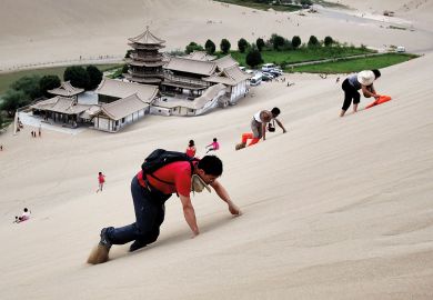 Tourists climb the Singing Sand Dunes near the Crescent Moon Spring