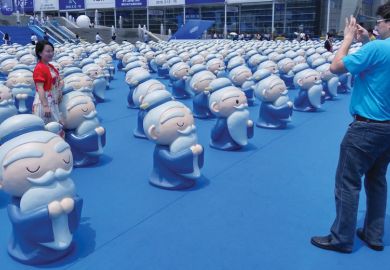Person standing with a confucius display as a metaphor for Germany too dependent on Confucius Institutes