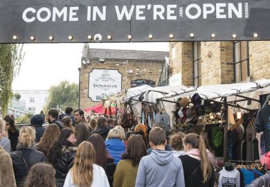 crowds passing under an entrance sign reading " Come in We're (very) Open. crowds passing under an entrance sign reading " Come in We're (very) Open.