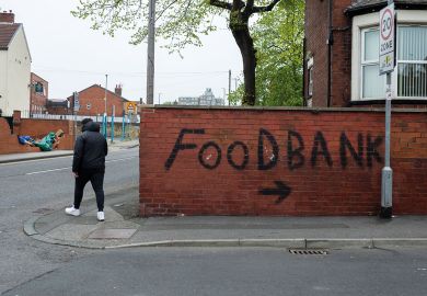 Person passes by bold, black graffiti that points towards a local food bank Person passes by bold, black graffiti that points towards a local food bank to illustrate that One in four UK universities now running a food bank