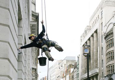 A man suspended from ropes.jpg Image of a man suspended from ropes cleans an office in central London as metaphor for that universities in London will be tipped into deficit or pushed further into the red