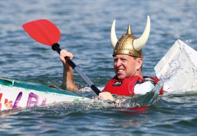 Person wearing viking hat in a cardboard boat sinking at a boat Regatta to illustrate the Danish humanities courses pressed on contact hours as funding cut
