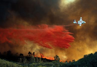 An airplane makes a fire retardant drop on a large hill-top home An airplane makes a fire retardant drop on a large hill-top home