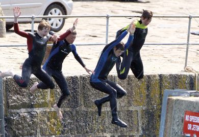 Four people jumping off from a harbour wall as a metaphor for cutting English fees and student numbers.