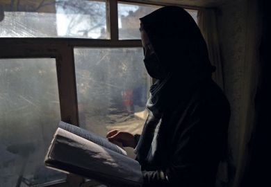 Marwa, a student at her home in Kabul reading next to a window as women are now banned from attending university in Taliban