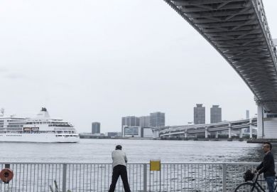 A man observes a ship passing under the Rainbow Bridge in Tokyo, Japan as a metaphor for Japan ‘will  miss the boat’  if it doesn’t  go global