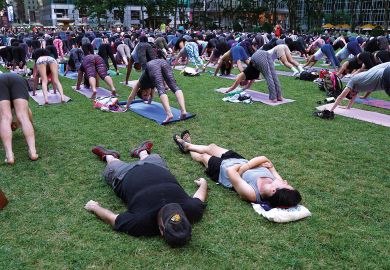 A couple of tourists nap in the grass as people participate in an outdoor yoga event to illustrate US universities mull adopting New York college’s four-day week