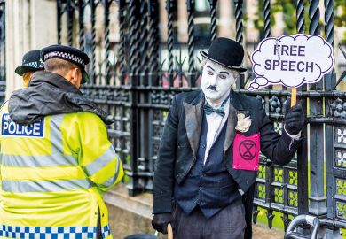Police question a protester dressed in Chaplin type clothes outside the Houses of Parliament London holding a Free Speech banner to illustrate Labour urged to outline free speech act future as criticism grows