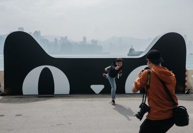 A man poses for a photograph in front of a billboard featuring the Tmall Cat, mascot for Alibaba Group Holding Ltd.'s Tmall online marketplace to illustrate Alibaba makes inroads in Europe