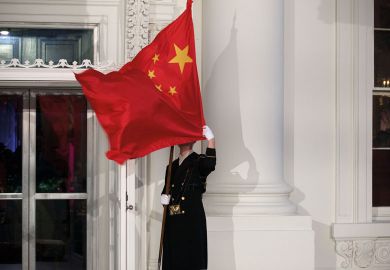 A military honor guard holds the Chinese flag in front of the White House in Washington which has blown over his face to illustrate Republicans target universities over China and political research