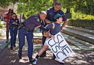 Holding a sign that said Sue USC a USC student is arrested by campus police in USC Village after calling for USC to sued and held accountable for their actions surrounding the pro-Palestinian protest on campus on Monday, May 6, 2024 in Los Angeles, CA 