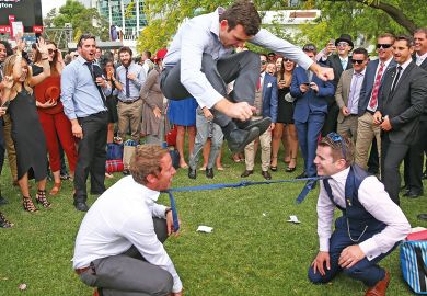  A man jumps over two men who have their ties tied together as they play a game of Limbo in Melbourne, Australia to illustrate Australian universities ‘already near’ overseas enrolment caps