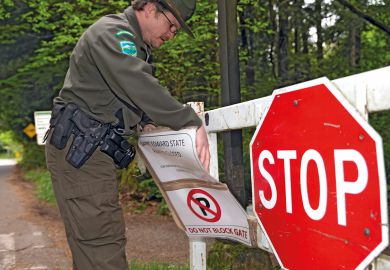 A ranger adjusts stop sign saying the park is closed in Kenmore, WA , Seattle to illustrate US college closures could spread to public universities