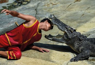 A performer putting his head between the gaping fangs of a crocodile to illustrate Florida universities quiet over ban on hiring Chinese academics