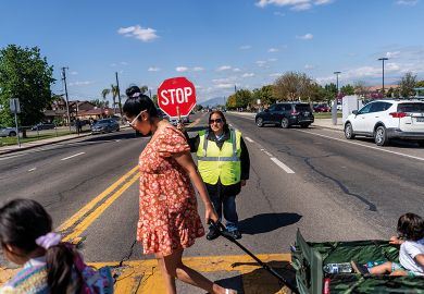 A crossing guard stops traffic as the school day ends in Cutler, California to illustrate State lawmakers launch push to end legacy admissions in US