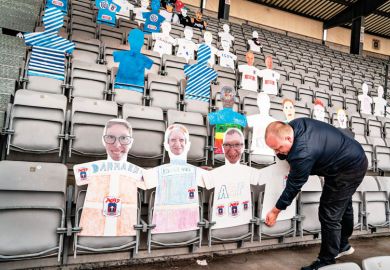 A man places cardboard figures with pictures of the fans in the empty tribunes of the Ceres Park Football Stadium