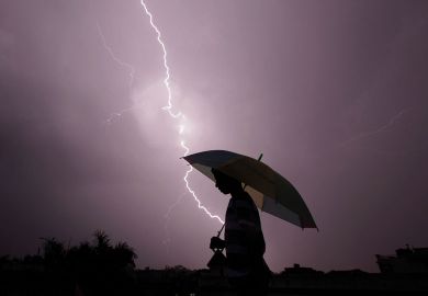 A pedestrian walks with an umbrella as lightning strikes to illustrate Pressure on Ashoka builds as intelligence services visit campus