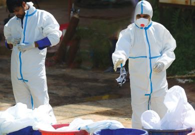 Two medical staff removing Personal Protective Equipment kits into a dustbin as a metaphor for universities reprioritising teaching over research.