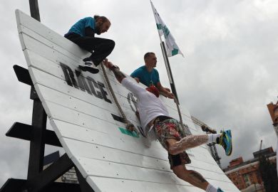 An athlete lends a helping hand to another contestant climbing up the warped wall 