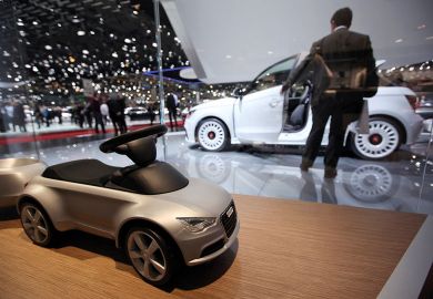 A toy car for Audi AG is seen on the company's stand with a man looking at white car in background A toy car for Audi AG is seen on the company's stand with a man looking at white car in background